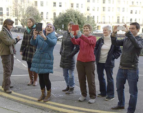 A group of volunteers and researchers testing VisAge software by holding up various mobile devices. In the background can be seen the Regency houses of Brunswicvk Square, Hove.